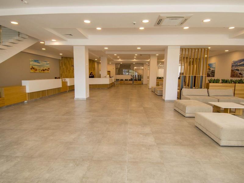 Großer heller Innenraum mit beigen Sofas, weißen Wänden, Treppe und moderner Beleuchtung.