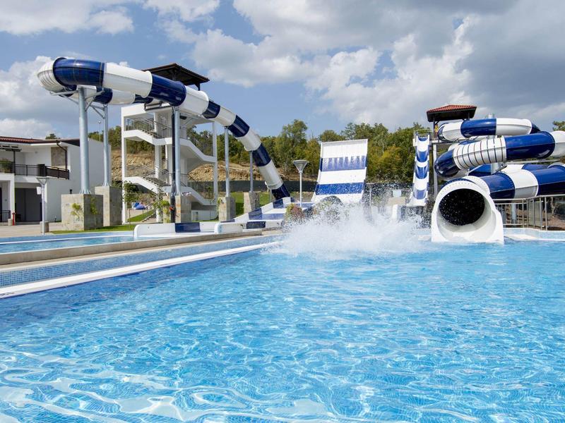 Freizeitbad mit mehreren blauen und weißen Wasserrutschen, klarem Wasser und bewölktem Himmel.