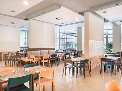 Ristorante d'hotel moderno e luminoso con sedie di legno e grandi finestre per molta luce naturale.