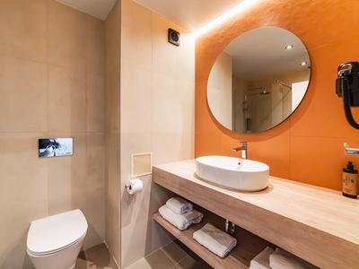 Bagno moderno con specchio rotondo, lavabo e WC in tonalità calde.