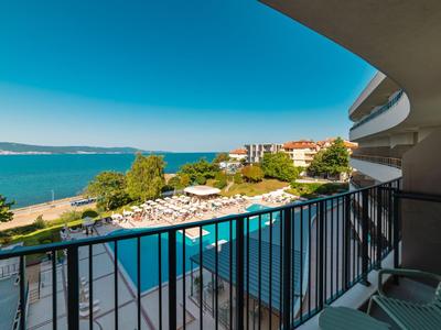 Balkon z widokiem na basen, leżaki i morze pod błękitnym niebem w hotelu.