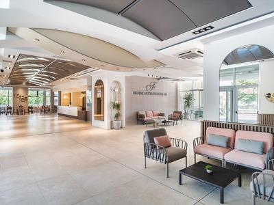 Ingresso di hotel luminoso con area salotto, arredi moderni e grandi finestre che lasciano entrare la luce naturale.