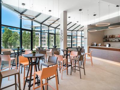Interno moderno di una caffetteria con pareti in vetro, molte sedie e un lungo bancone del bar.