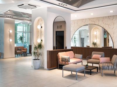 Area lounge elegante dell'hotel con poltrone moderne, grande finestra ad arco e illuminazione calda.