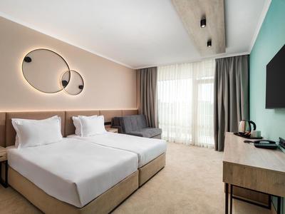 Camera d'hotel moderna con due letti singoli, divano, scrivania e TV a muro.