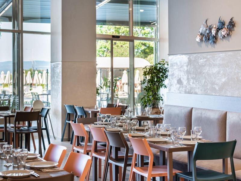 Ristorante luminoso con arredamento moderno in legno e grandi finestre con vista sul giardino.