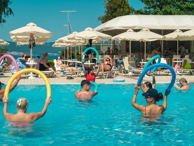 Persone nella piscina dell'hotel che galleggiano con anelli colorati sotto ombrelloni.