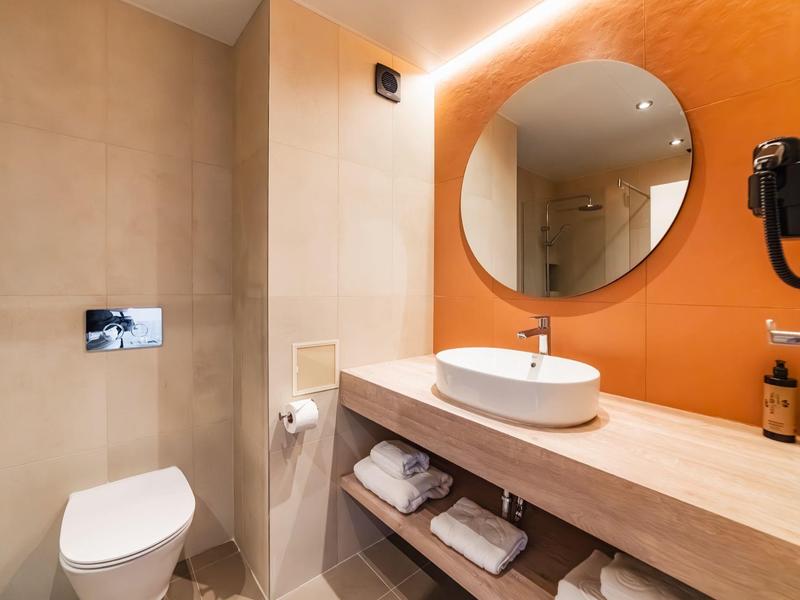 Bagno moderno con specchio rotondo, lavabo e WC in tonalità calde.
