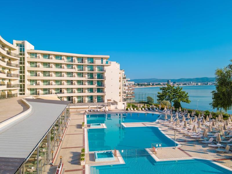 Grande piscina dell'hotel con lettini e vista sul mare sotto un cielo limpido.