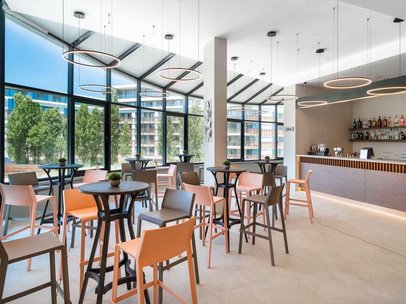 Interno moderno di una caffetteria con pareti in vetro, molte sedie e un lungo bancone del bar.