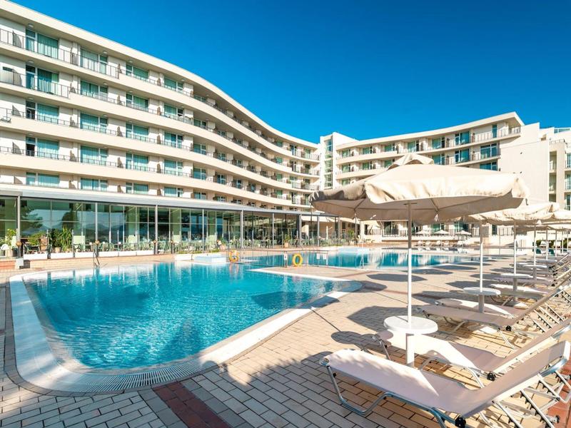 Piscina moderna dell'hotel con lettini e grandi ombrelloni sotto un cielo azzurro