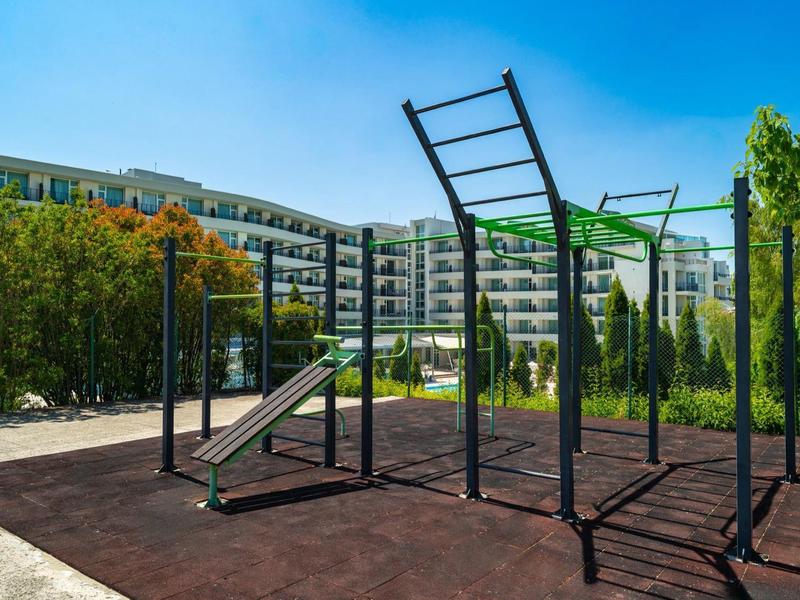 Area fitness esterna moderna con sbarre per trazioni e scivolo davanti a un edificio hotel.