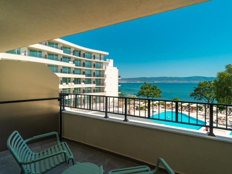 Balcone con sedie con vista su hotel, piscina e mare sotto un cielo terso.