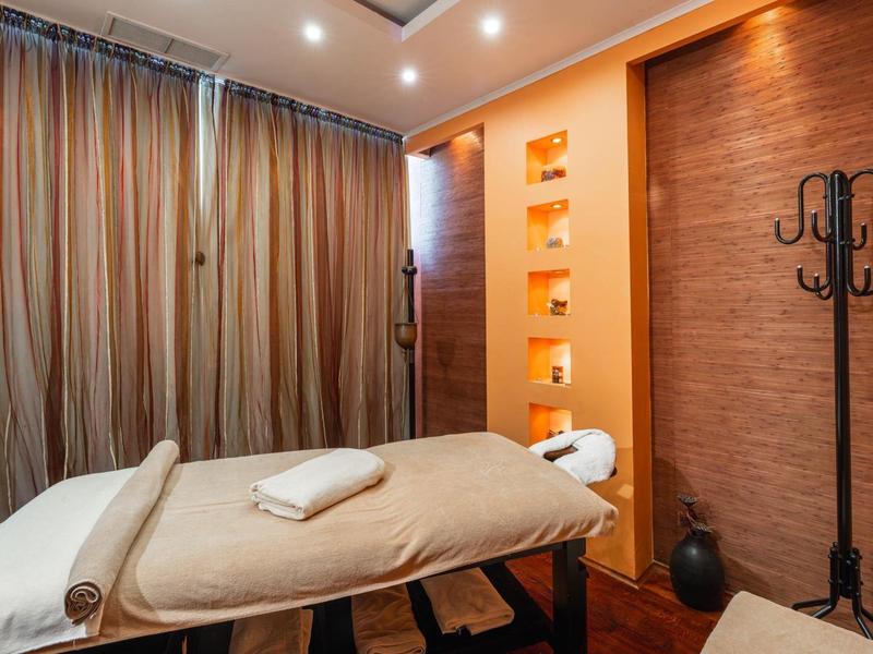 Accogliente stanza per trattamenti con lettino da massaggio, tende morbide e luce calda.