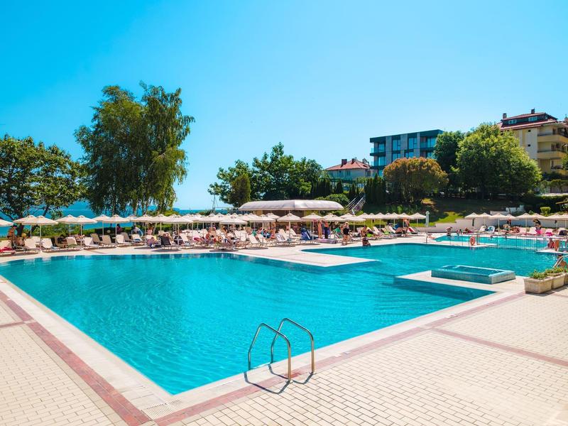Grande piscina all'aperto con lettini e ombrelloni sotto un cielo sereno in un resort.