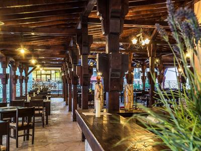 Rustikales Restaurant mit Holzdecke, Statuen und dekorativen Pflanzen in warmem Licht.