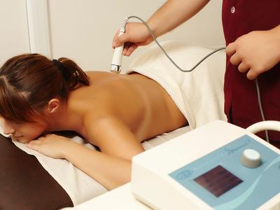 Frau erhält Rückenmassage mit elektrischem Therapiegerät in entspannter Ambiente.