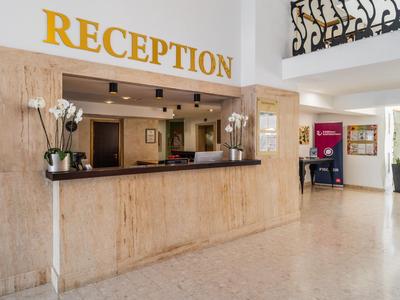 Helle Hotelrezeption mit Marmortheke, Blumenarrangement und dekorativem Geländer.