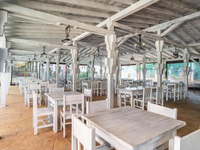 Helle, offene Terrasse mit weißen Holztischen und Stühlen in einem Hotelrestaurant.