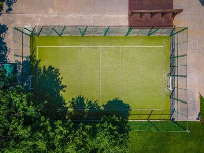 Überblick eines Tennisplatzes mit grünem Belag, umgeben von Zäunen und Bäumen.