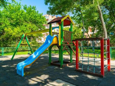 Bunter Kinderspielplatz mit Rutsche in einem sonnigen, grünen Hotelgarten.