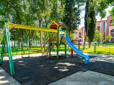 Bunter Kinderspielplatz mit Rutsche und Schaukel im Park neben Hotelgebäuden.
