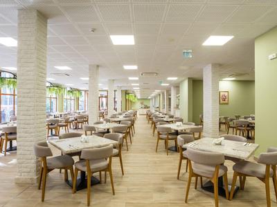 Großer, heller Hotel-Esseraum mit modernen Holztischen und grauen Stühlen.