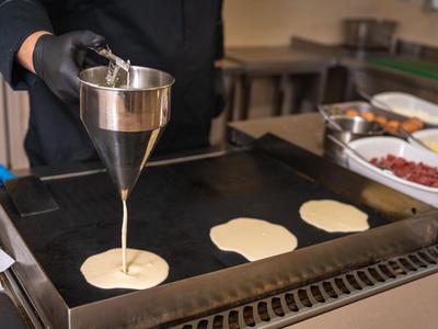 Ein Koch gießt Teig auf eine heiße Grillplatte in einer Küche.
