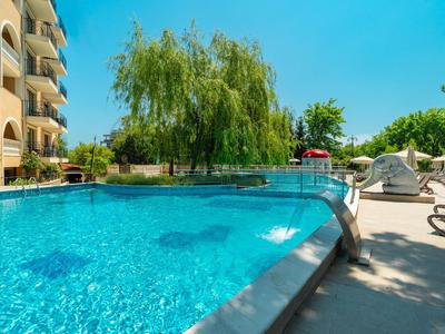 Hotelpool mit klar blauem Wasser, umgeben von Liegestühlen und Bäumen unter klarem Himmel.