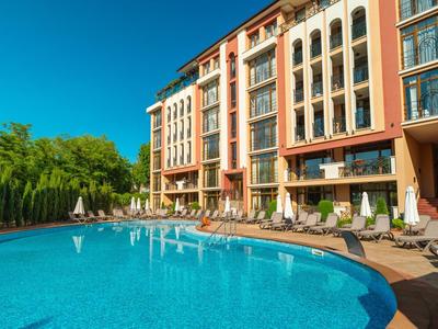 Großes Hotel mit Außenpool, Sonnenliegen und Sonnenschirmen unter blauem Himmel.