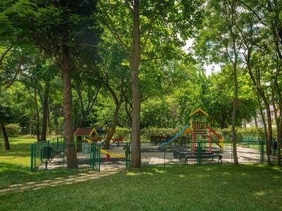 Spielplatz mit Rutschen und Klettergerüsten umgeben von Bäumen in einem gepflegten Park.