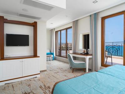 Moderner Hotelzimmer mit blauem Bett, Schreibtisch mit Stuhl und Balkon mit Meerblick.