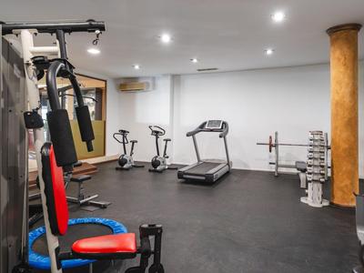 Moderner Fitnessraum mit verschiedenen Trainingsgeräten, Laufband und Hanteln in einem Hotel.