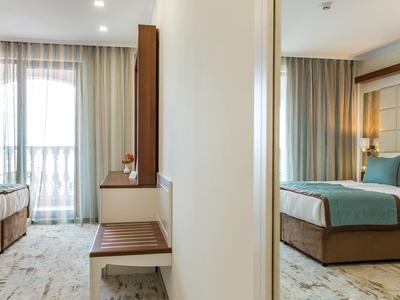 Moderner Hotelzimmerbereich mit Bett, Fenster und Vorhängen, geteilt durch eine Wand.
