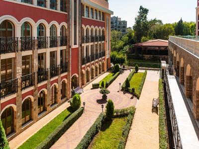 Innenhof eines Hotels mit gepflegten Wegen, Hecken und Blumenbeeten zwischen zwei Gebäuden.