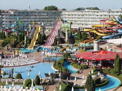 Waterpark met kleurrijke glijbanen, zwembaden en ligstoelen bij een resortgebouw.