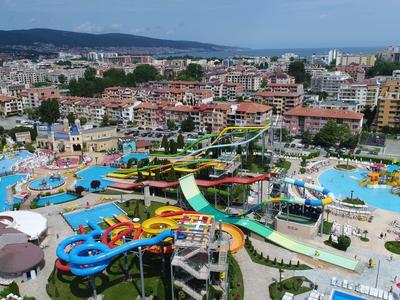 Groot waterpark met glijbanen en zwembaden bij stadsgebouwen en heuvels op de achtergrond.