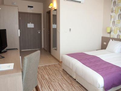 Moderne hotelkamer met tweepersoonsbed, paarse bedloper, bureau en wand-tv.