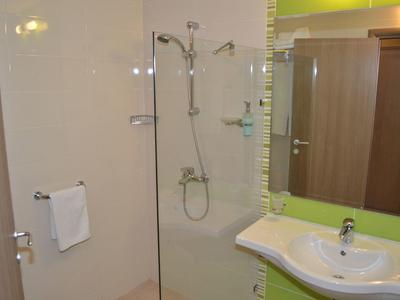 Kleine hotelbadkamer met glazen douche, witte wasbak, handdoekrek en houten kast.