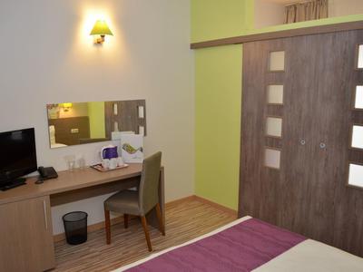 Hotelkamer met bureau, stoel, tv en bed met paarse deken, houten vloer en schuifdeur.