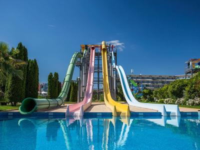 Bunte Wasserrutschen, verschiedene Formen, enden in großem blauen Pool, umgeben von grünen Pflanzen.