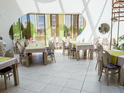 Světle zařízená jídelna s velkými okny a moderním nábytkem.