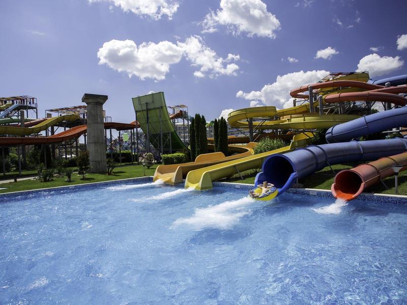 Glijbanen die uitkomen in een zwembad bij zonnig weer met wolken.