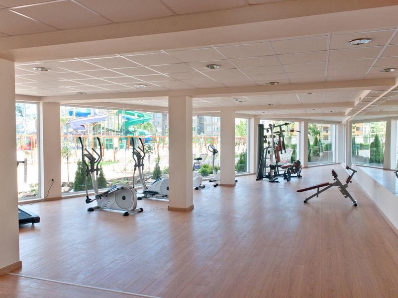 Lichte sportschool met hometrainers, gewichten en grote ramen met uitzicht op de tuin.