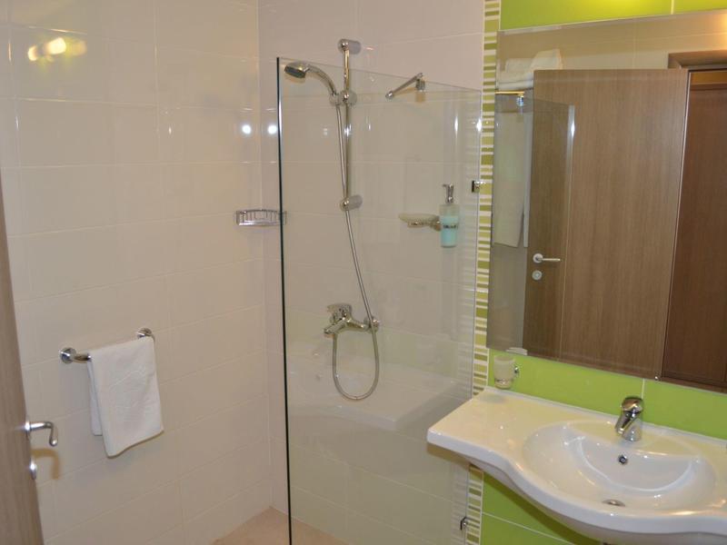 Kleine hotelbadkamer met glazen douche, witte wasbak, handdoekrek en houten kast.