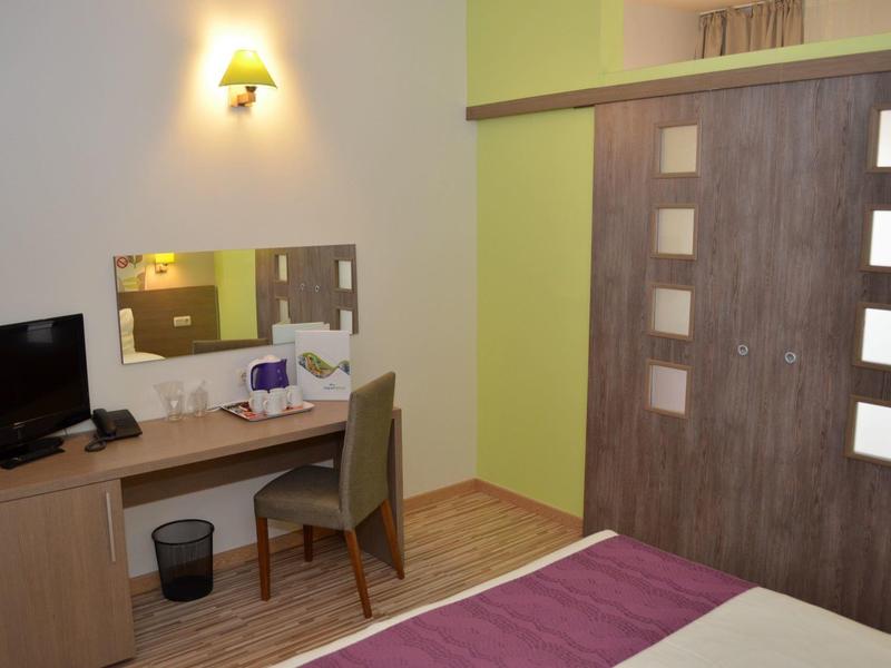 Hotelkamer met bureau, stoel, tv en bed met paarse deken, houten vloer en schuifdeur.