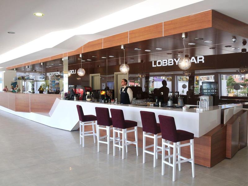 Moderne hotel lobbybar met een lange witte bar en meerdere paarse stoelen.