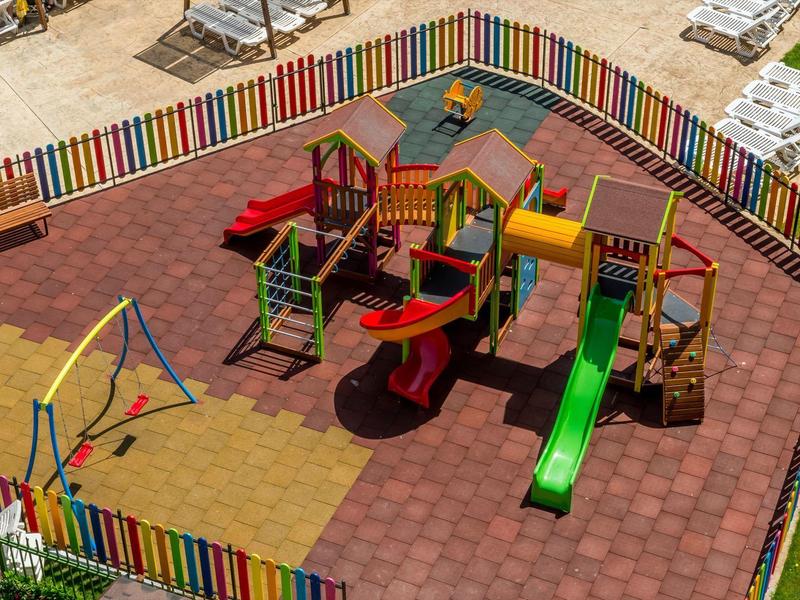 Kleurrijke speeltuin met glijbanen, schommels en klimtoestellen omringd door een veelkleurig hek.