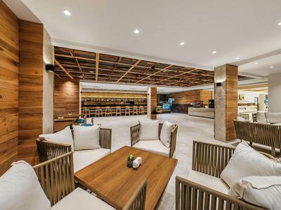 Moderna zona de descanso de hotel con paredes de madera y sillones blancos alrededor de una mesa de madera.