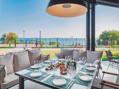 Table à manger sur terrasse avec vue sur parc et mer sous ciel clair.